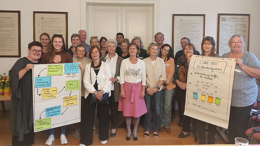 Gruppenfoto von gut 20 Personen in einem Büroraum, die Personen am linken bzw. rechten Rand der Gruppe halten jeweils ein Flipchart in die Kamera