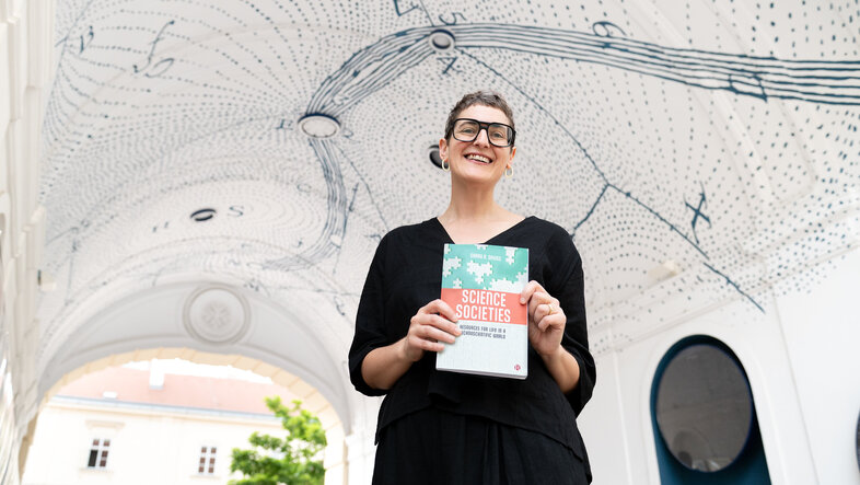 Portrait aus der Forschperspektive. Die Autorin hält das Buch in beiden Händen vor dem Körper.